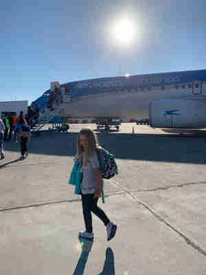 Child standing in front of an airplane on the tarmac with the sun behind them