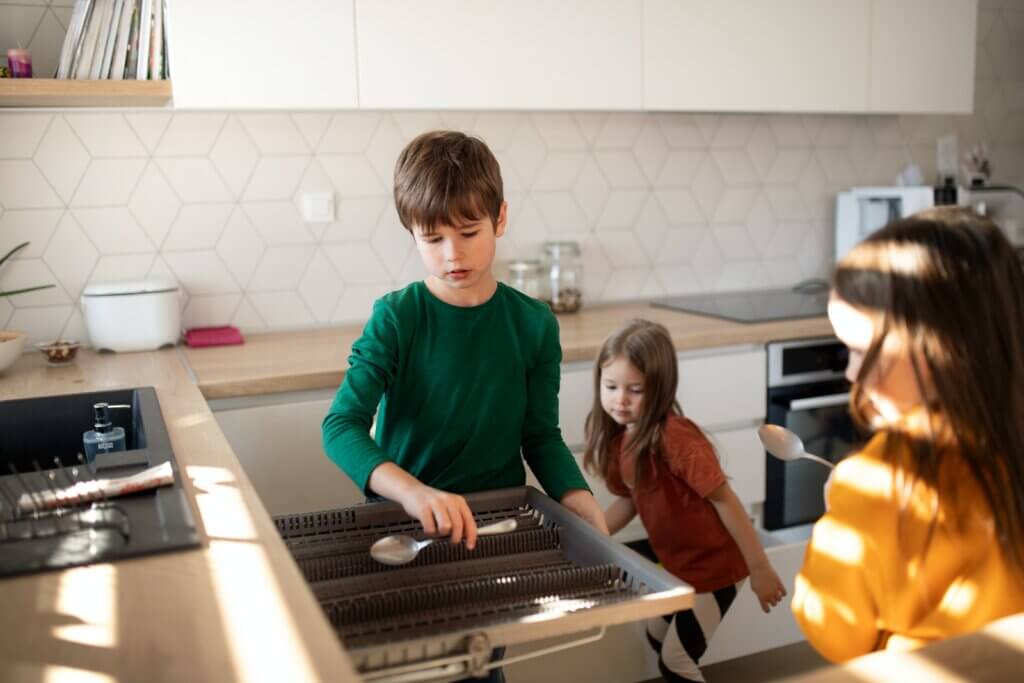 Three children putting dishes away from a dishwasher.
